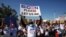 FILE - Migrants from Central America and other nationalities, hoping to cross and request asylum in the U.S., hold banners and shout slogans to U.S. President Joe Biden at their campsite, in Tijuana, Mexico, Feb. 27, 2021.