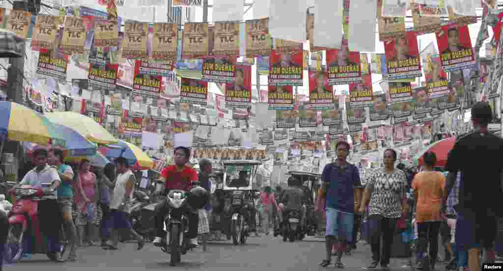 Election posters for the midterm elections hang along a street as residents walk to a polling precinct in Taguig, Metro Manila, May 13, 2013. 