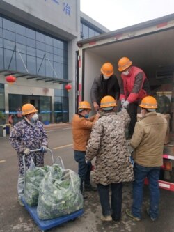 FILE - Construction workers building a temporary hospital receive meat and vegetables delivered by Wuhan resident Chen Hui and another volunteer in Ezhou, Hubei province, China, Feb. 11, 2020.