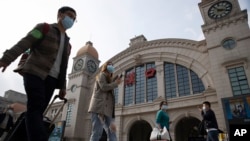 Travelers with their luggage walk past the Hankou railway station on the eve of its resuming outbound traffic in Wuhan in central China's Hubei province on April 7, 2020.