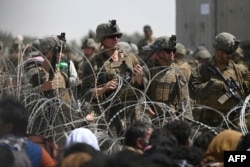 U.S soldiers stand guard behind barbed wire as Afghans sit on a roadside near the military part of the airport in Kabul, Aug. 20, 2021, hoping to flee from the country after the Taliban takeover of Afghanistan.