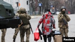 A woman walks past Ukrainian military service members guarding a road that leads to a government block, after Russian President Vladimir Putin authorized a military operation in eastern Ukraine, in Kyiv, Ukraine, Feb. 24, 2022.