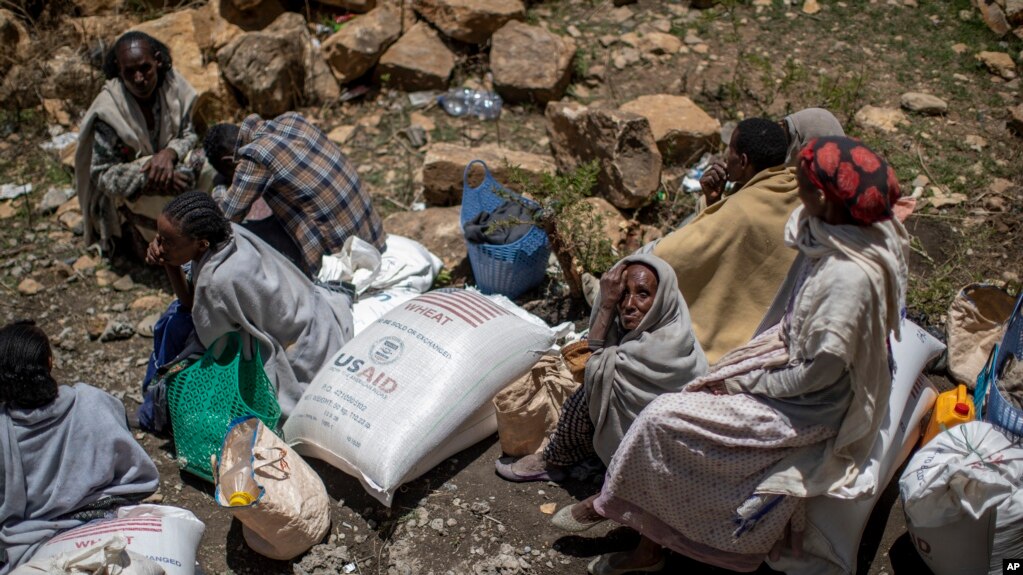 FILE - An elderly Ethiopian woman sits with others next to a sack of wheat donated to conflict victims in the town of Agula, in the Tigray region of northern Ethiopia, May 8, 2021.