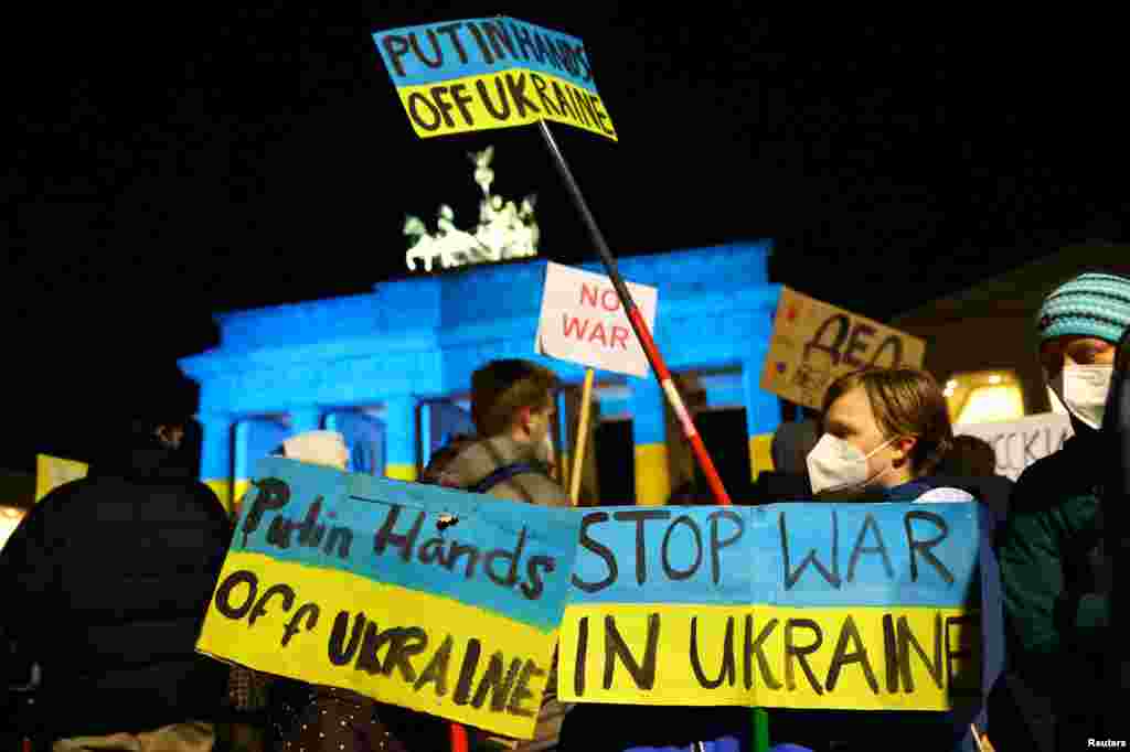 Personas llevan pancartas frente a la Puerta de Brandenburgo iluminadas con los colores de la bandera ucraniana durante una protesta en Berlín, Alemania, el 24 de febrero de 2022.