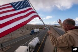 Para pendukung menyemangati para pengemudi pengemudi truk dan pengemudi lainnya yang tersesat di Needles, California, saat konvoi menuju Washington D.C. untuk berpartisipasi dalam aksi protes mandat COVID-19, Rabu, 23 Februari 2022. (AP Photo/Nathan Howard)