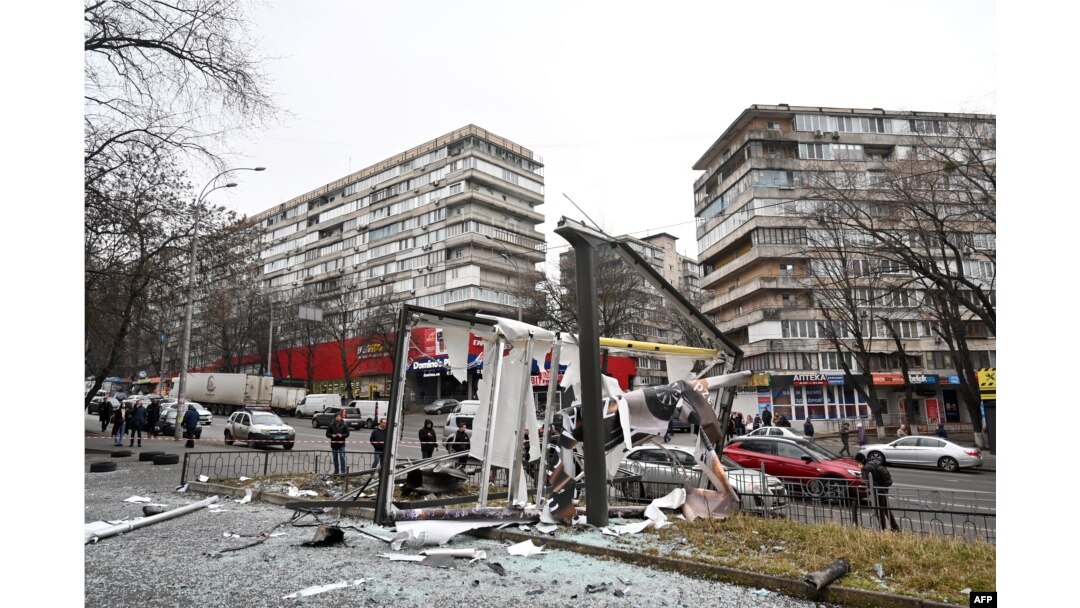 People are seen outside the cordoned-off area around the remains of a shell in a street in Kyiv, Feb. 24, 2022.