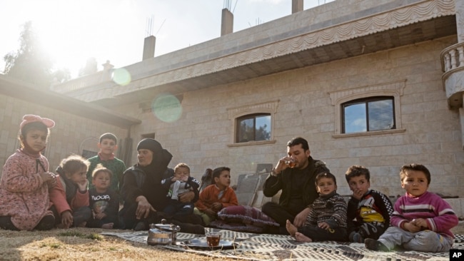 Milhem Daher drinks tea as he sits with his family outside his house in Raqqa province, Syria, Monday, Feb. 7, 2022. Raqqa, the former capital of the IS caliphate and home to about 300,000, is now free, but many of its residents try to leave. (AP Photo/Baderkhan Ahmad)