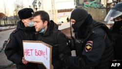 Police officers detain a man holding a placard reading "No to war!" during a protest against Russia's invasion of Ukraine, at Moscow's Pushkin Square, Feb. 24, 2022.