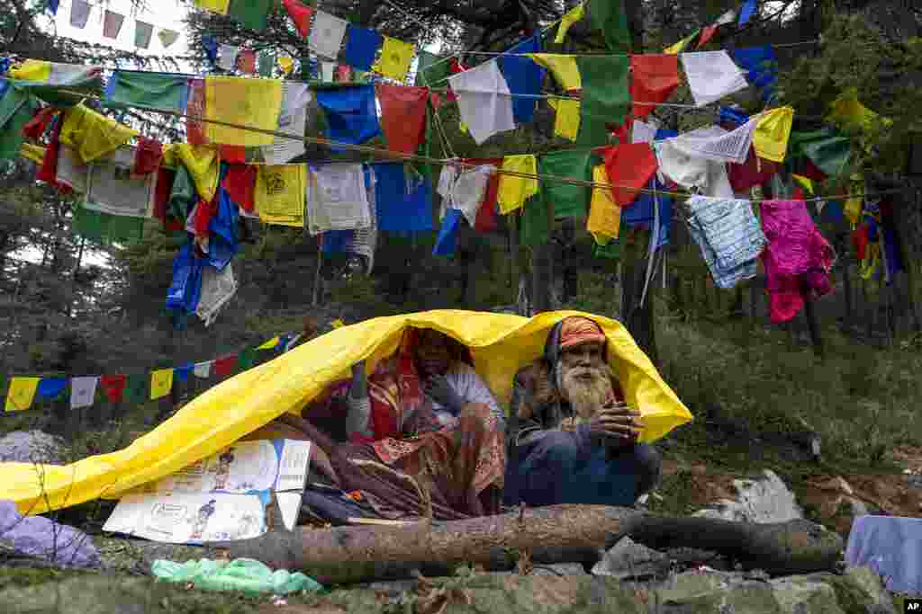 A man and a woman cover themselves with tarpaulin to stay dry under a rainfall in Dharmsala, India.