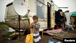 FILE - A girl leans on a school back pack outside a caravan at an encampment of Roma families in Triel-sur-Seine, near Paris, France.