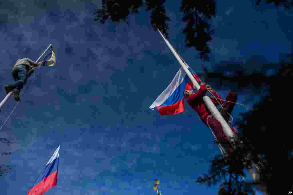 Seorang anggota pasukan pro-Rusia menurunkan bendera Angkatan Laut Ukraina (kiri) saat yang rekannya mengibarkan bendera Rusia di Markas Besar Angkatan Laut Ukraina di Sevastopol. Krimea, 19 Maret 2014.