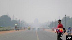 India's Presidential Palace, in the backdrop, is covered with smog as a roadside vendor crosses Rajapth, the ceremonial boulevard in New Delhi,Oct. 16, 2019.