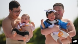 FILE - Held by college sumo wrestlers, a couple of babies cry in their Naki Sumo or Crying Baby Contest at Sensoji Buddhist temple in Tokyo.