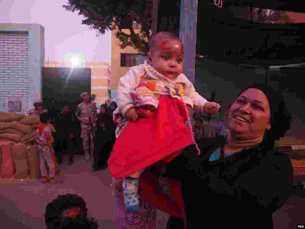 Outside a polling station, a woman holds up her baby with “C.C.” painted on her forehead to demonstrate her support for President Abdel Fattah el-Sissi, in Cairo, Egypt, Dec. 1, 2015. (Photo - H. Elrasam/VOA)