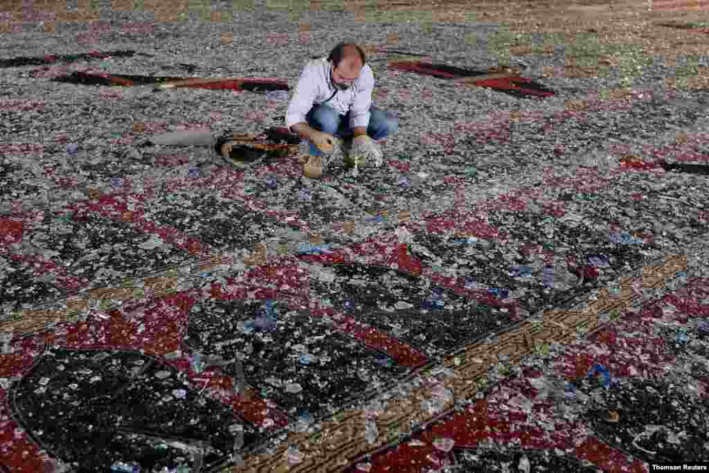 폭발로 파손된 레바논 베이루트의 사원에서 한 남성이 카펫 위에 떨어진 유리 조각들을 치우고 있다.