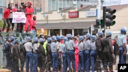 Zimbabwean police officers keep an eye on opposition party supporters as they prepare to march during a protest aimed at President Robert Mugabe in Harare, March, 14, 2016.