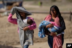 Mujeres cargan bebés después de llegar en bote desde la mina La Bulla Loca, que colapsó, en La Paragua, estado Bolívar, Venezuela, el viernes 23 de febrero de 2024. (Foto AP/Ariana Cubillos)