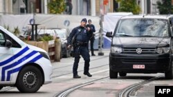 ব্রাসেলসের শেরবিক এলাকায় একটি বাড়ির সামনে পাহারা দেওয়ার সময় এক পুলিশ কর্মকর্তা ইশারা করছেন, যেখানে ব্রাসেলসে হামলার সন্দেহভাজন অপরাধী পুলিশের অভিযানে গুলিবিদ্ধ হয়ে মারা যায় । (১৭ অক্টোবর, ২০২৩