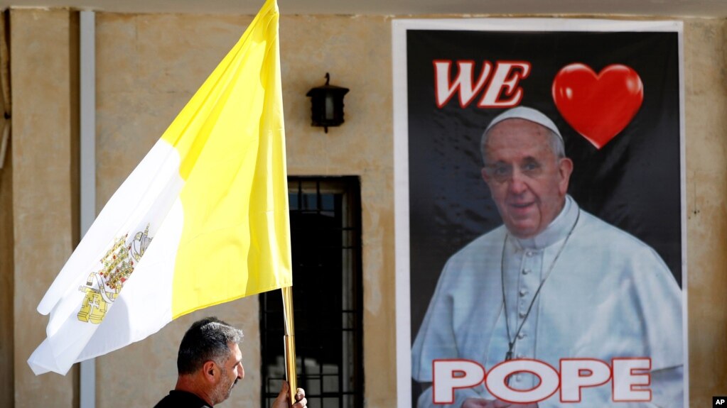 A Christian priest holds a Vatican flag as he walks past a poster of Pope Francis during preparations for the Pope's visit in Mar Youssif Church in Baghdad, Iraq, Feb. 26, 2021.
