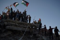 Protesters wave Palestinian flags as they stand atop the rubble of a building destroyed by an Israeli airstrike last month, during a protest against a march by Jewish ultranationalists through east Jerusalem, June 15, 2021.