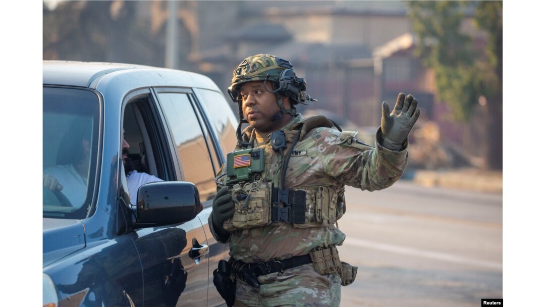 A National Guardsman talks with a driver near damaged structures burned from a wildfire in Altadena, California, on Jan. 10, 2025.