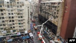 This picture taken and released by Taiwan’s Central News Agency (CNA) on October 14, 2021 shows rescue operations after an overnight fire tore through a building (pictured R) in the southern Taiwanese city of Kaohsiung, killing at least 46 people and injuring dozens of others.
