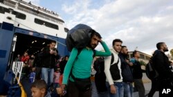 A man carries his belongings as other migrants and refugees arrive on a ferry from the Greek island of Lesbos at the Athens' port of Piraeus, Sept. 30, 2015. 