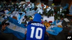 A fan mourns in front of flowers and posters left in tribute to Diego Maradona at the entrance of the Boca Juniors stadium known as La Bombonera in Buenos Aires, Argentina, Nov. 27, 2020. Maradona died Nov. 25 at age 60.