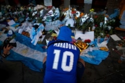 A fan mourns in front of flowers and posters left in tribute to Diego Maradona at the entrance of the Boca Juniors stadium known as La Bombonera in Buenos Aires, Argentina, Nov. 27, 2020. Maradona died Nov. 25 at age 60.