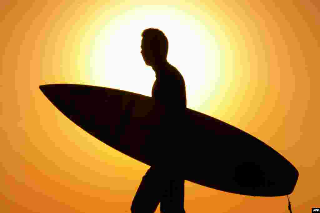 An Israeli surfer walks on the beach in the coastal city of Netanya, north of Tel Aviv, as the sun sets over the Mediterranean Sea.