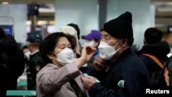 A woman wearing a mask to prevent contracting the coronavirus adjusts her husband's mask as they wait to check in at Incheon International Airport in Incheon, South Korea, March 19, 2020. REUTERS/Kim Hong-Ji