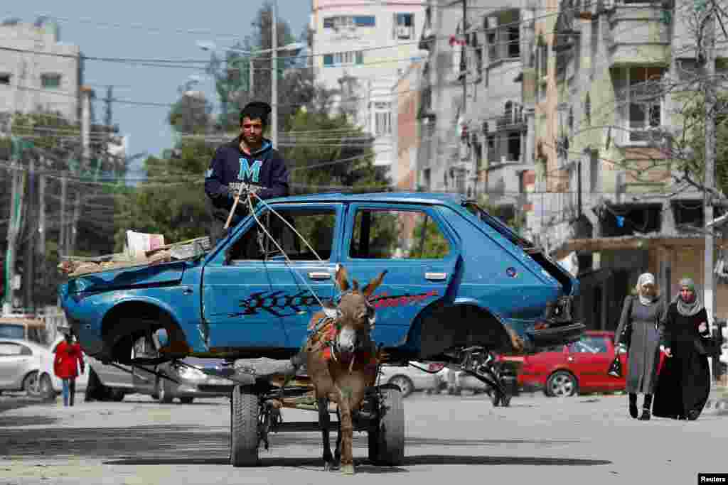 A Palestinian man rides a donkey-drawn cart transporting an old car to a scrap yard, in Gaza City.
