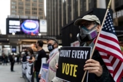 FILE - A man wearing a protective mask due to COVID-19 pandemic holds a sign outside Madison Square Garden, which is used as a polling station, on the first day of early voting in Manhattan, New York, October 24, 2020.