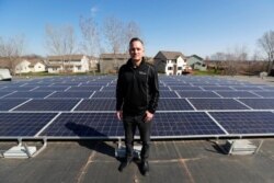 FILE - Todd Miller stands next to solar panels on the roof of his solar installation business in Ankeny, Iowa, April 15, 2019.