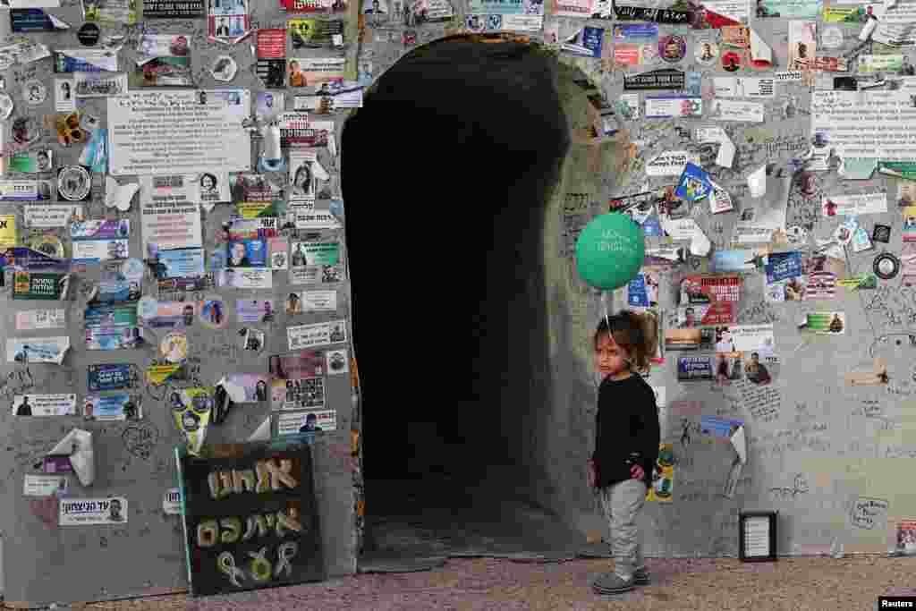 A child holds a balloon in front of an installation representing a Hamas tunnel, with a memorial wall at the entrance, as supporters of hostages kidnapped Oct. 7, 2023, by Hamas call for their release, in Tel Aviv, Israel.