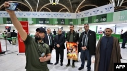 A man takes a selfie with people holding a portrait of slain Hezbollah leader Hassan Nasrallah before boarding a flight to Beirut at the Baghdad International Airport on Feb. 20, 2025. Thousands of Nasrallah's supporters are traveling to Lebanon for his funeral on Feb. 23.