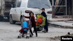 FILE - Children push containers in strollers as they flee deeper into the remaining rebel-held areas of Aleppo, Syria, Dec. 12, 2016. 