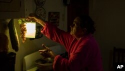 Marta Bermudez Robles, 66, hangs a lamp in her kitchen in Adjuntas, Puerto Rico, at her home that is still with electricity since Hurricane Irma and Maria, July 12, 2018.