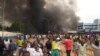 FILE - With the headquarters of the ruling party burning in the back, supporters of mutinous soldiers demonstrate in Niamey, Niger, Thursday, July 27 2023.