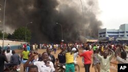 FILE - With the headquarters of the ruling party burning in the back, supporters of mutinous soldiers demonstrate in Niamey, Niger, Thursday, July 27 2023.
