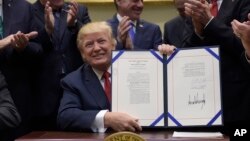 President Donald Trump hold up the Veterans Choice Program Extension and Improvement Act that he signed, April 19, 2017, in the Roosevelt Room of the White House in Washington.