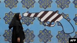 An Iranian woman walks past a mural depicting a gun painted on the wall of the former US embassy in the capital Tehran.