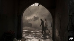 FILE - Construction workers carry a generator as a bulldozer removes debris from destroyed shops in the Old City of Mosul, Iraq, Nov. 18, 2017.