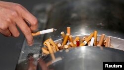 A man flicks ashes from his cigarette over a dustbin in Shanghai January 10, 2014. Korean scientists are looking to turn the cigarette butts into carbon material for batteries.