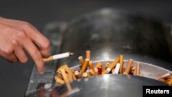 FILE - A man flicks ashes from his cigarette over a dustbin in Shanghai January 10, 2014. 