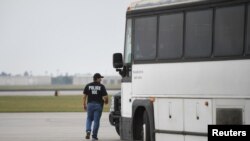 Un oficial de inmigración de EE. UU. camina al lado de un bus para transportar inmigrantes que serán deportados desde el aeropuerto internacional de Brownsville, Texas, en mayo de 2018.