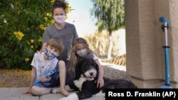 Christie Black, middle, with her two children, Angela and Luke, left, and the family dog Teddy, pose at their home, Tuesday, May 11, 2021, in Mesa, Ariz. (AP Photo/Ross D. Franklin) 