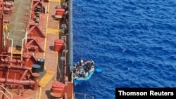 FILE - Migrants sit in a boat alongside the Maersk Etienne tanker off the coast of Malta, in this handout image provided Aug. 19, 2020. 