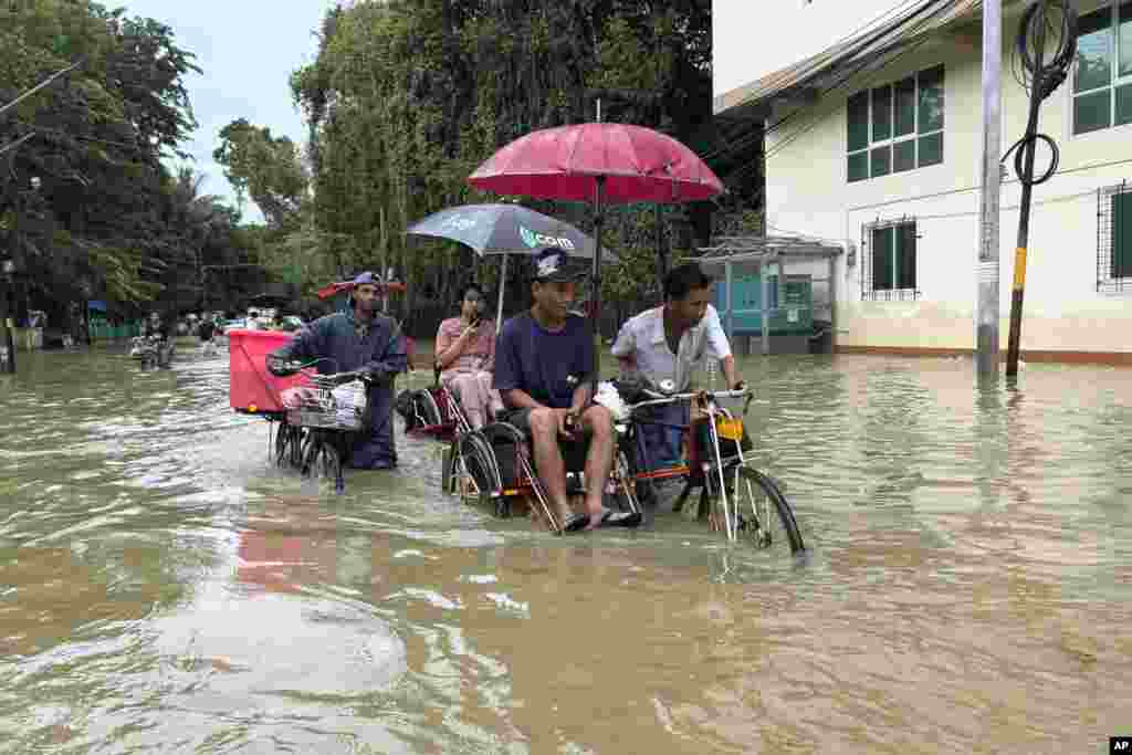 Passengers on trishaws move through a road flooded by heavy rain, in Yangon, Myanmar.