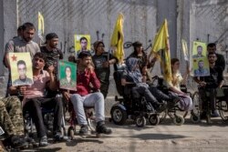 Wounded Kurdish fighters hold portraits of comrades who were killed fighting against IS militants, during a demonstration outside the U.N. building in Qamishli, northeast Syria, against an anticipated Turkish incursion, Oct. 8, 2019.